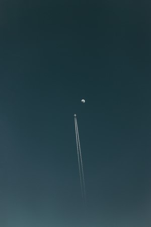 Airplane flying towards the Moon with contrails