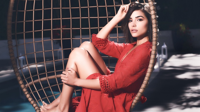 Olivia Culpo in a red dress sitting in a hanging chair