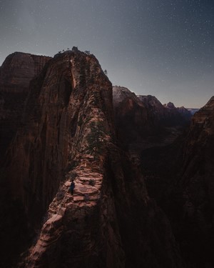 Hiker on narrow mountain ridge under starry sky