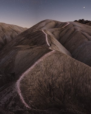 Person walking on a path through hills under the night sky