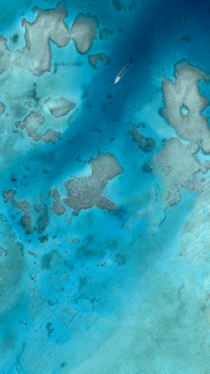 Aerial view of a boat sailing through turquoise coral reefs