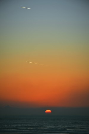 Sunset over the sea with contrails in the sky