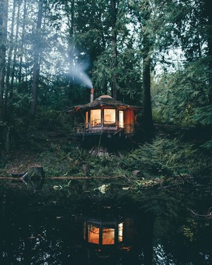 Cabin in the forest with smoke and water reflection