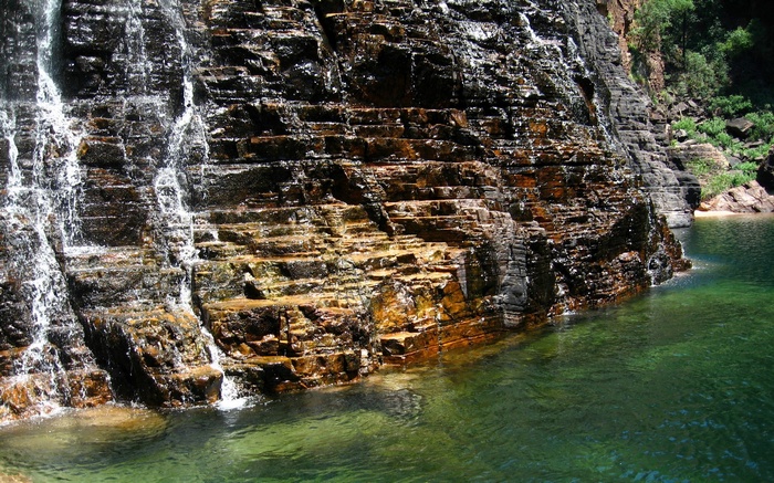 Waterfall cascading over layered rock into clear green water
