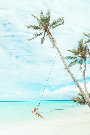 Woman on a swing under palm trees at a tropical beach