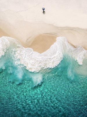 Aerial view of a person with an umbrella on a beach with turquoise waves