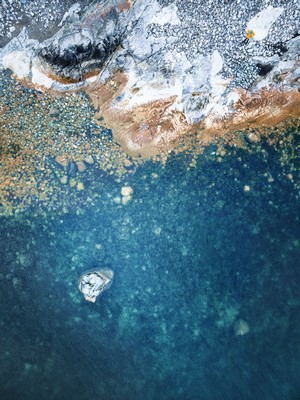 Aerial view of rocky shore meeting blue water