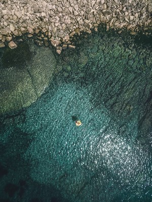 Person floating on a raft in clear teal water near rocky shore