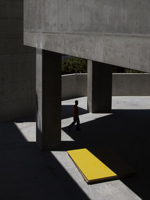 Man walking near concrete pillars and yellow board