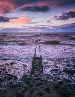 Waves crashing on a rocky shore with a pier at sunset