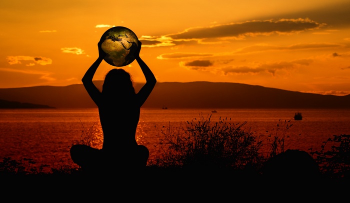 Woman holding Earth silhouette at sunset