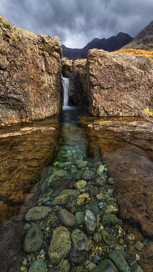 Waterfall flowing between rocks with mountains in the background