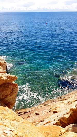 Rocky coast overlooking clear blue sea with a buoy