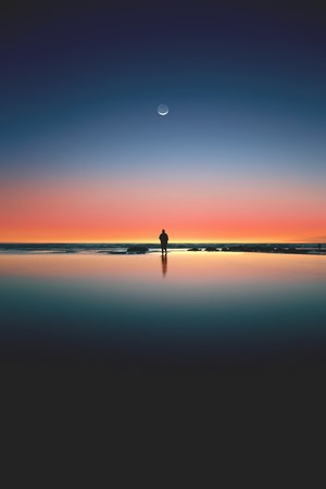 Silhouette of a person on a beach at sunset with a crescent moon