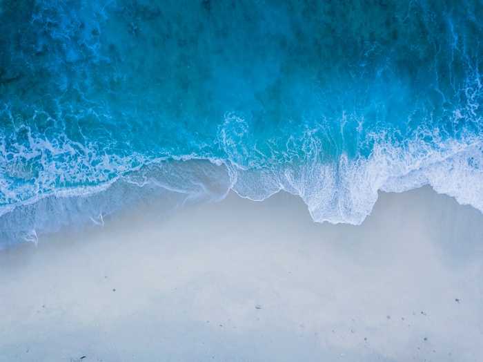 Aerial view of blue ocean waves crashing on a sandy beach, 4K