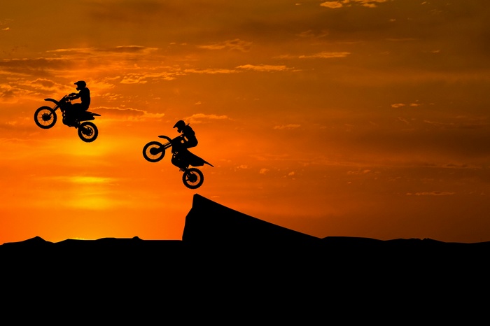 Motocross riders performing stunts at sunset