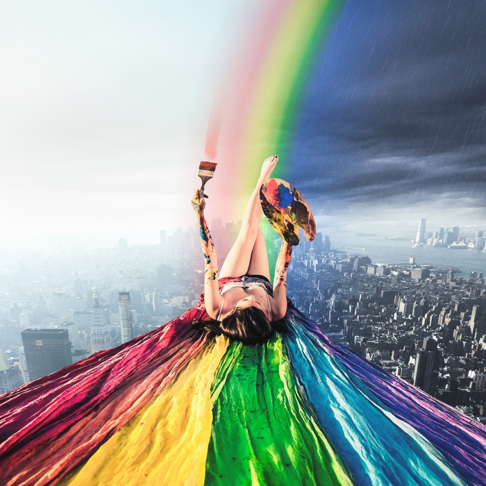 Woman painting a rainbow over a cityscape