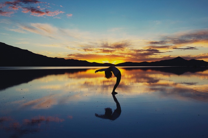 Silhouette of a person doing a backbend at sunset over a reflective body of water