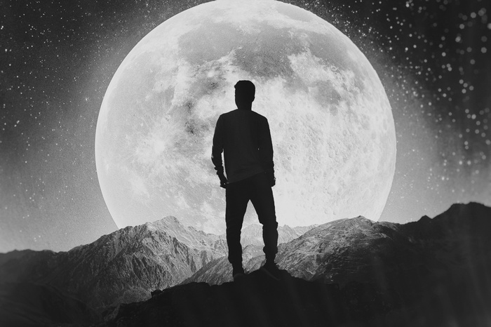 Silhouette of a man standing on mountains with a large moon