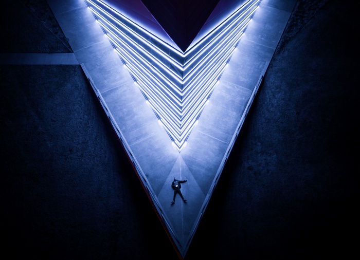 Man lying down in a V-shaped structure with neon lights