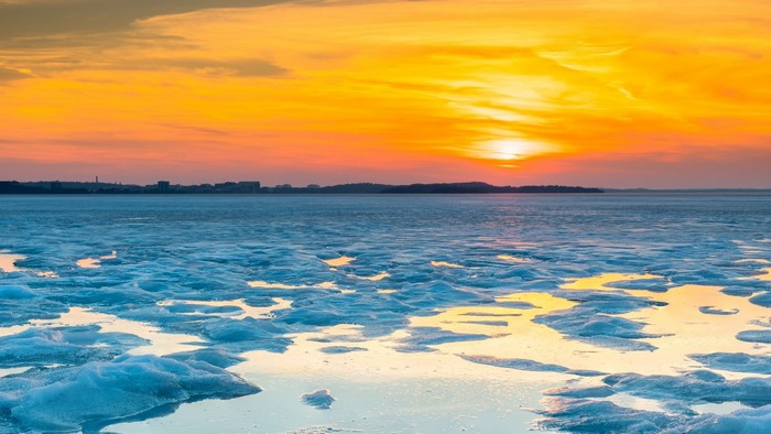 Sunset over icy water with city skyline