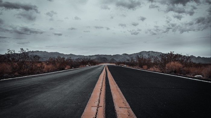 Desert road with mountains under cloudy sky