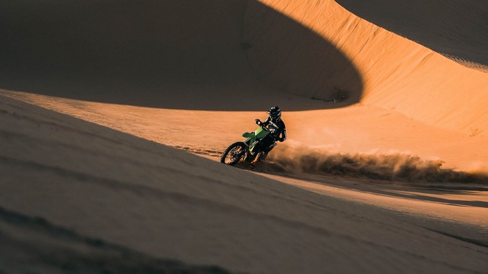 Motorcyclist riding a green dirt bike on a sand dune