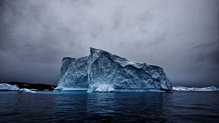 Large iceberg in dark ocean under cloudy sky