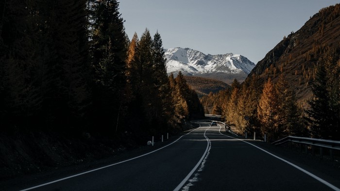 Winding mountain road through autumn forest with snow-capped peaks