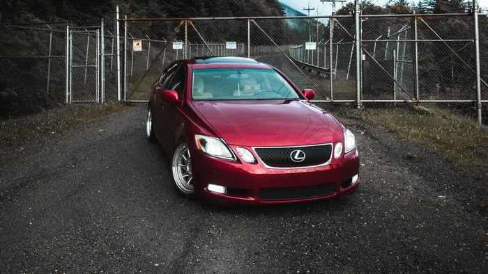 Red Lexus GS parked near a chain-link fence