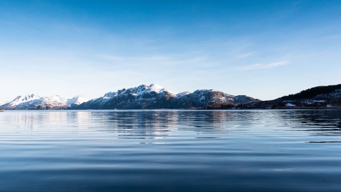 Snow-capped mountains reflected in calm water under a blue sky