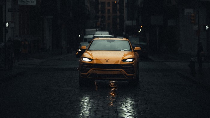 Yellow Lamborghini Urus driving on wet city street