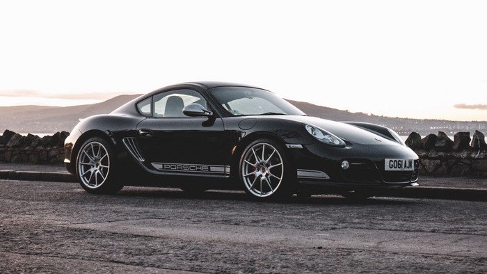 Black Porsche Cayman 987 R parked by a stone wall