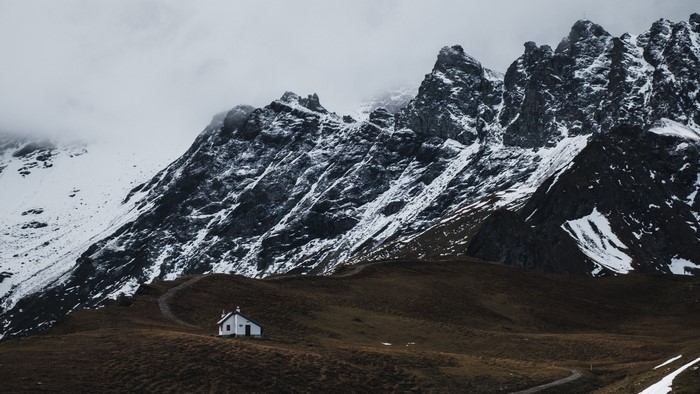 Small white chapel on a grassy hill with snow-capped mountains