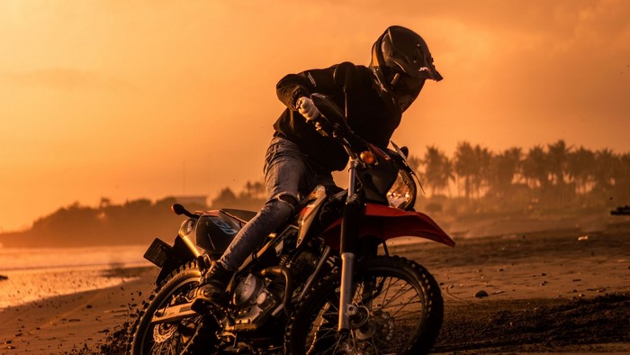Motorcyclist riding a dirt bike on a beach at sunset