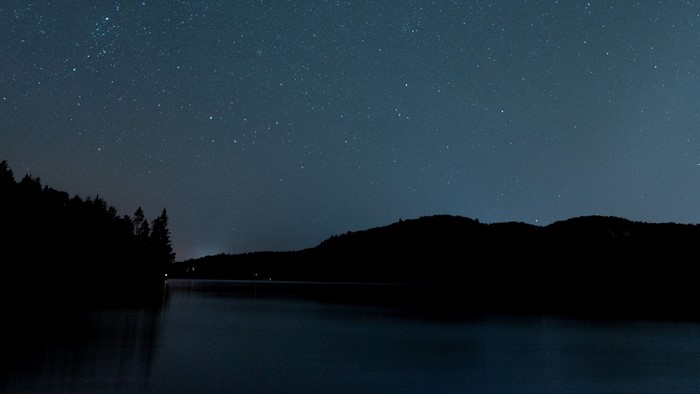 Night sky over a lake with silhouetted trees and hills