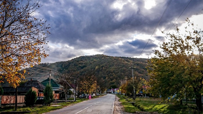 Autumn road through a village with a hill