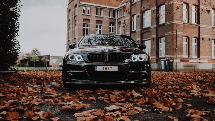 Black BMW M3 in front of brick building with autumn leaves