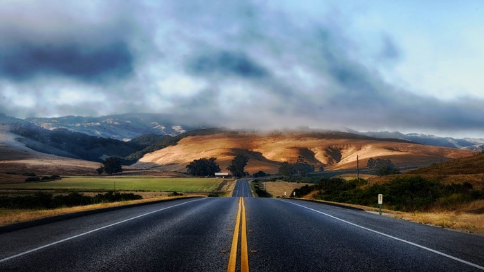 Road leading to rolling hills under cloudy sky
