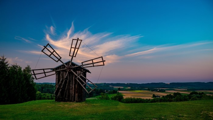 Old wooden windmill on a grassy hill at sunset