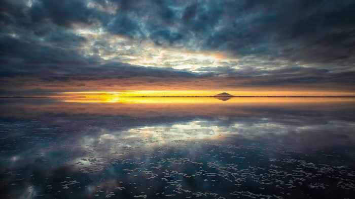 Sunset over a reflective salt flat with clouds