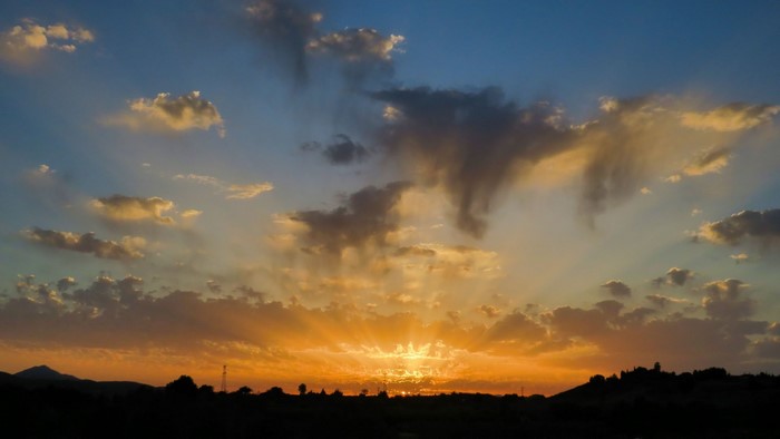 Sunset with sun rays over a silhouetted landscape