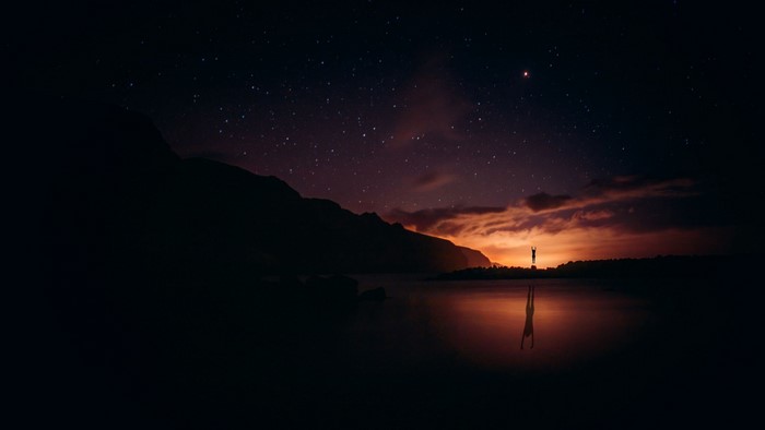 Person doing a handstand by a lake at sunset