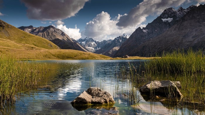 Mountain lake with grassy shore and rocky mountains