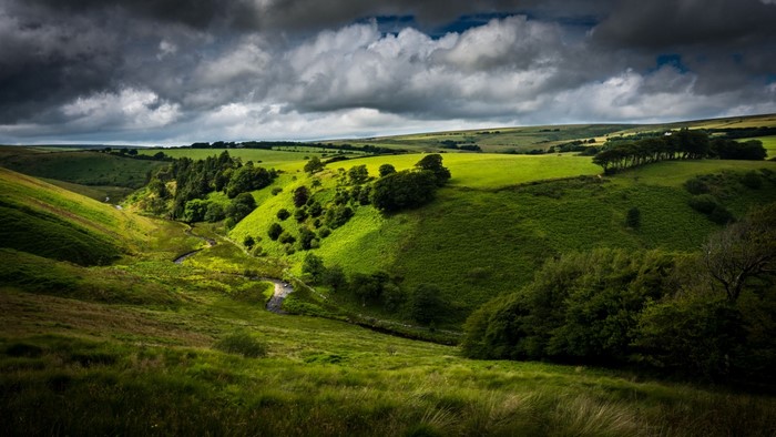 Rolling green hills with a winding stream under a cloudy sky