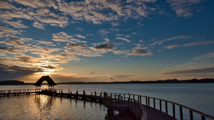 Wooden pier with a gazebo over a lake at sunset