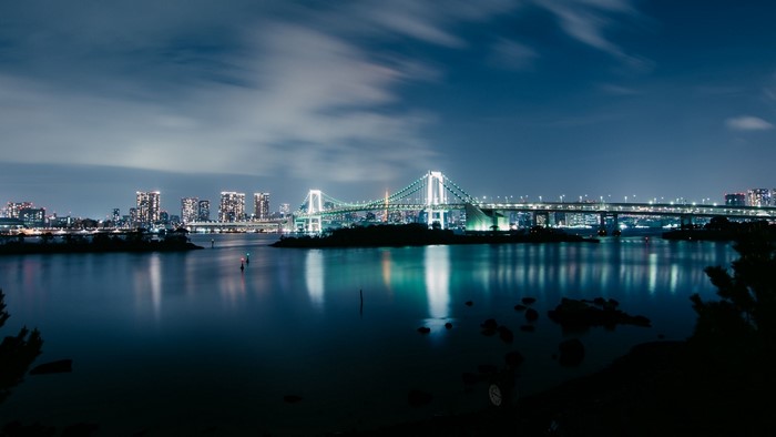 Rainbow Bridge at night over water with city skyline