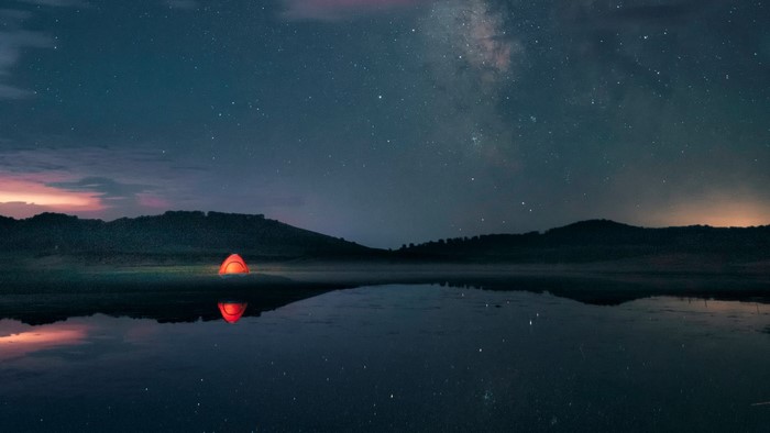 Tent by lake under starry night sky