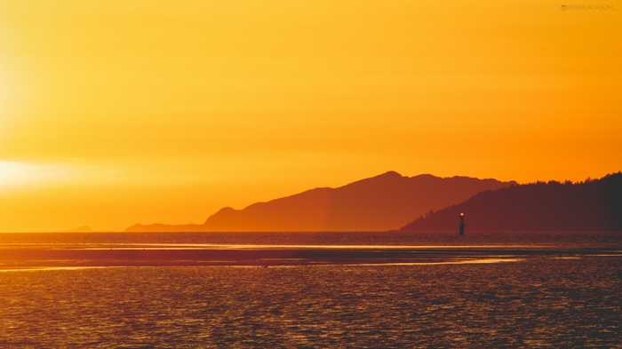 Sunset over the ocean with mountains and lighthouse
