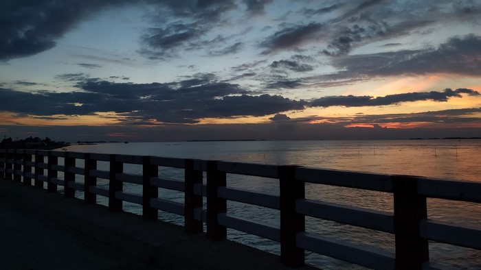 Sunset over the ocean with a bridge railing